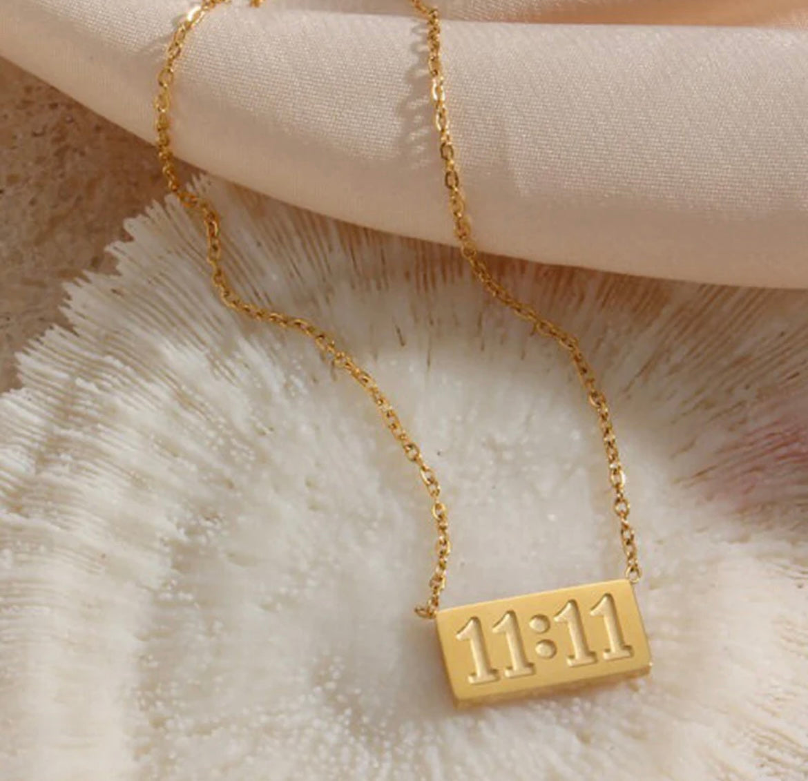 Gold 11:11 pendant necklace with delicate chain on textured white shell background