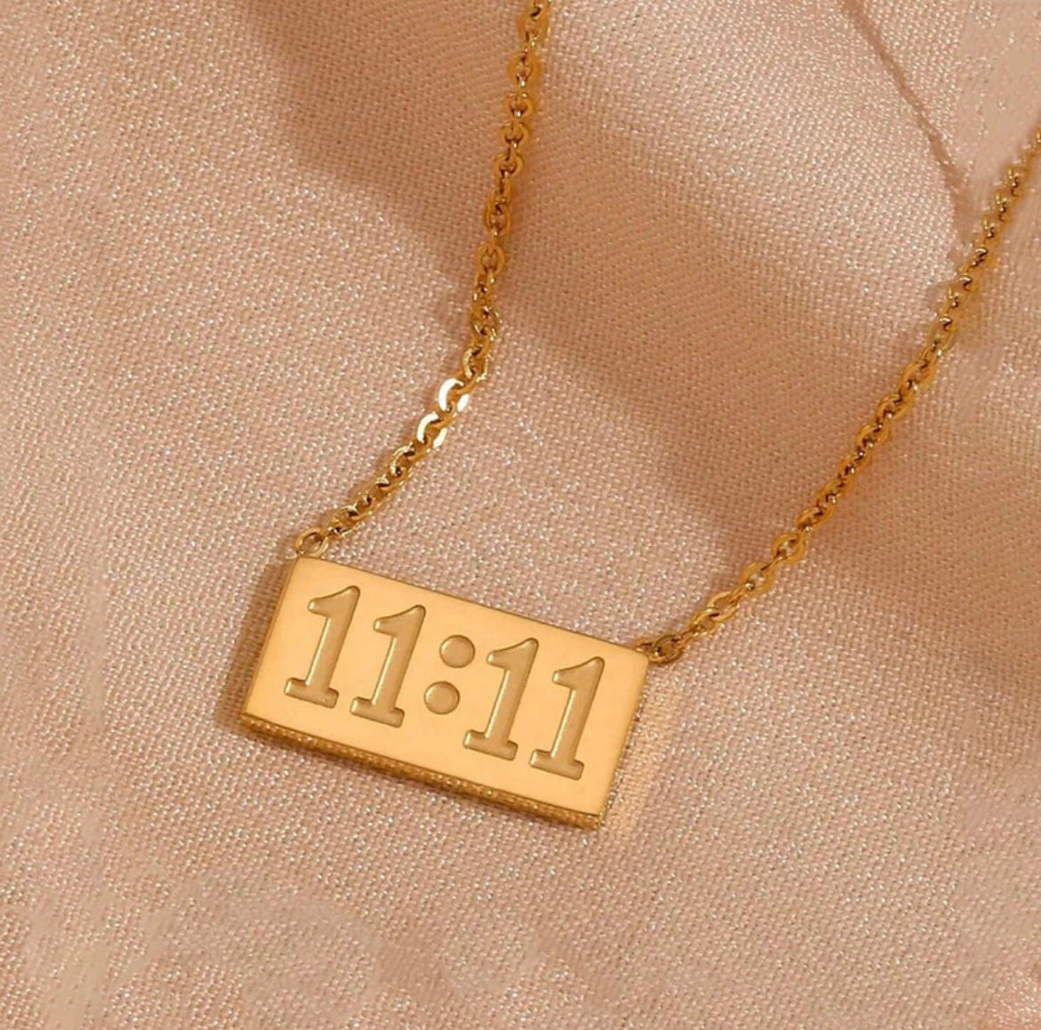 Gold 11:11 rectangular pendant necklace from ELL DESIGNS with a delicate chain on beige fabric
