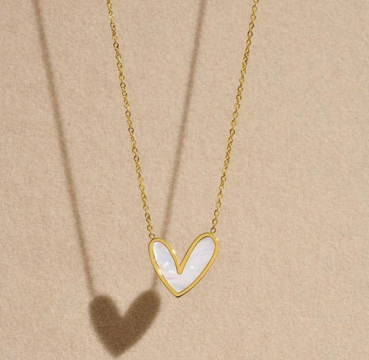 ELL DESIGNS gold chain necklace with white heart-shaped pendant casting shadow on beige background