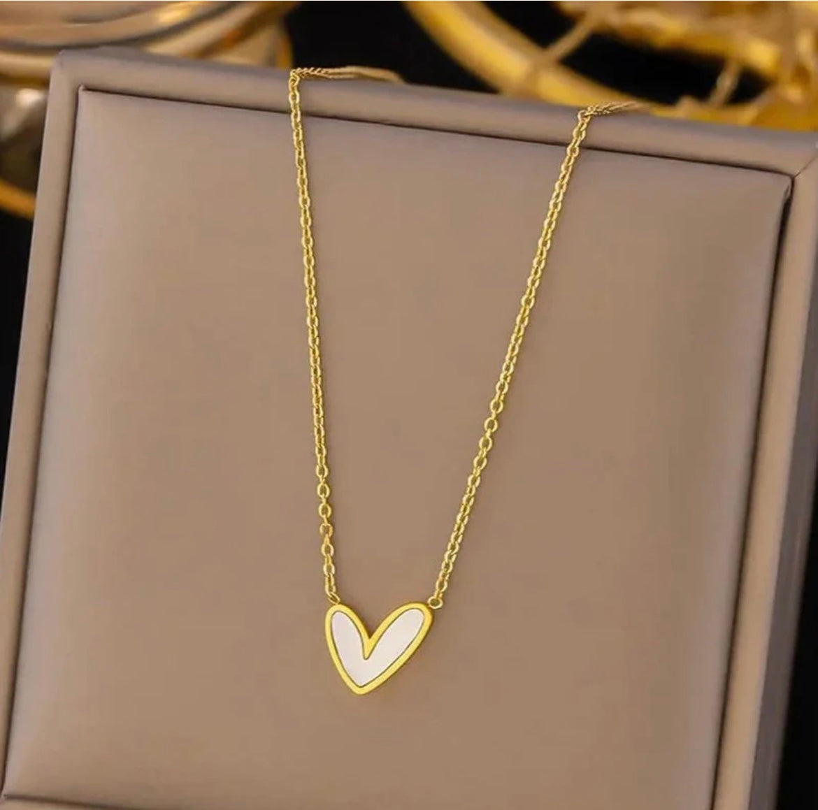 Gold chain necklace with a white enamel heart pendant on a beige jewelry display