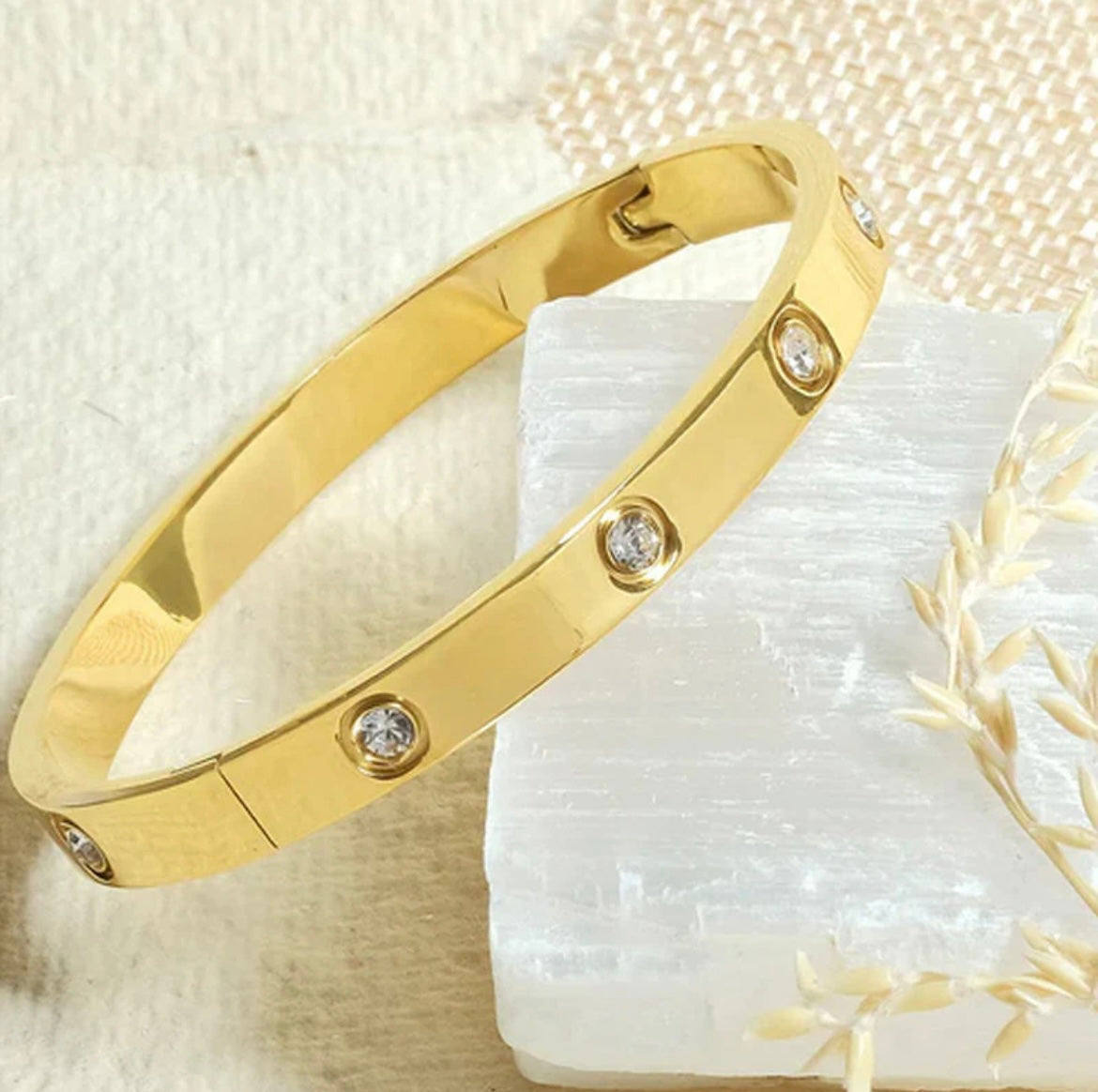 ELL DESIGNS gold bangle bracelet with embedded clear gemstones on textured background
