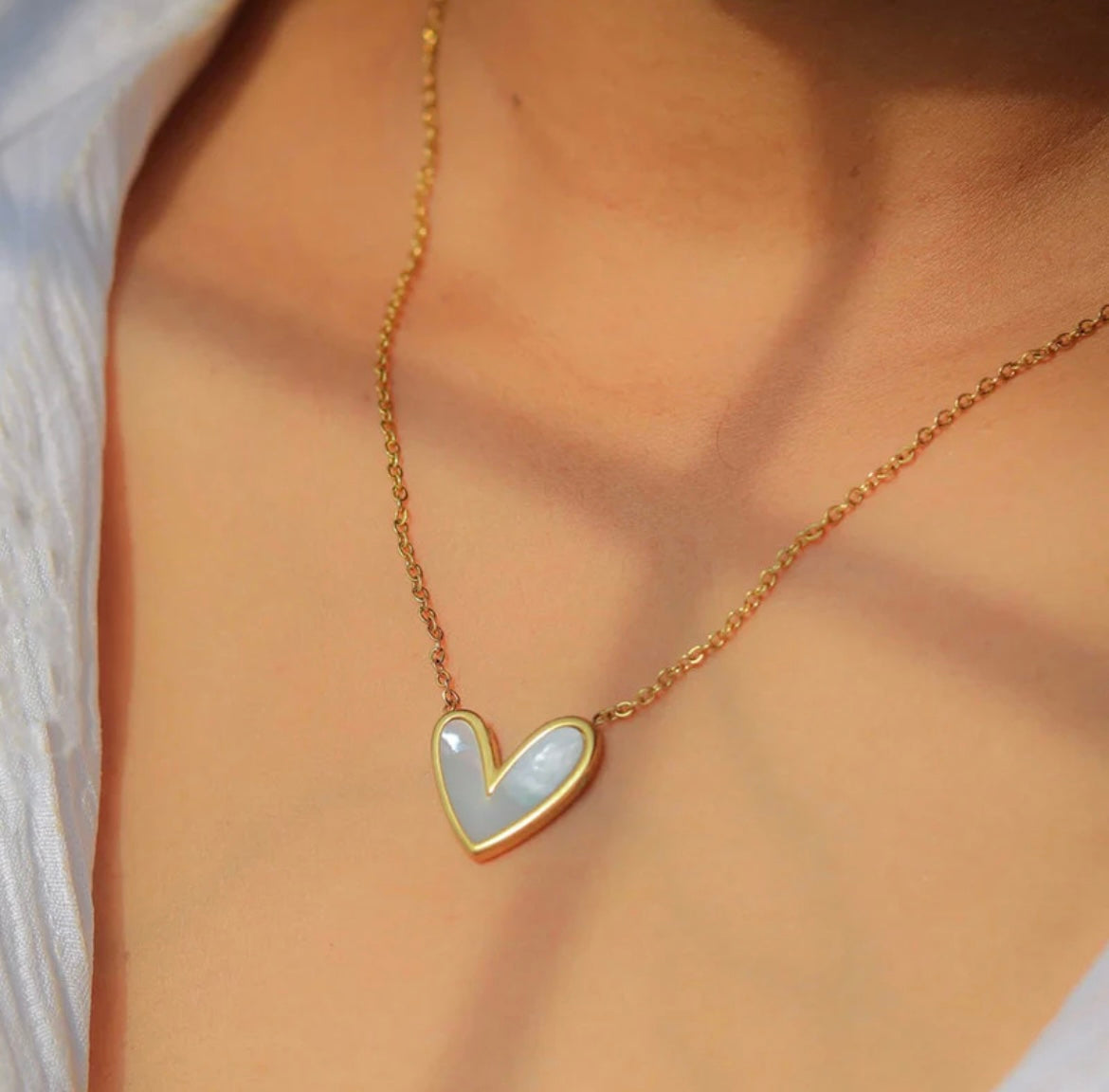 Gold chain necklace with white mother of pearl heart pendant by ELL DESIGNS worn on neck