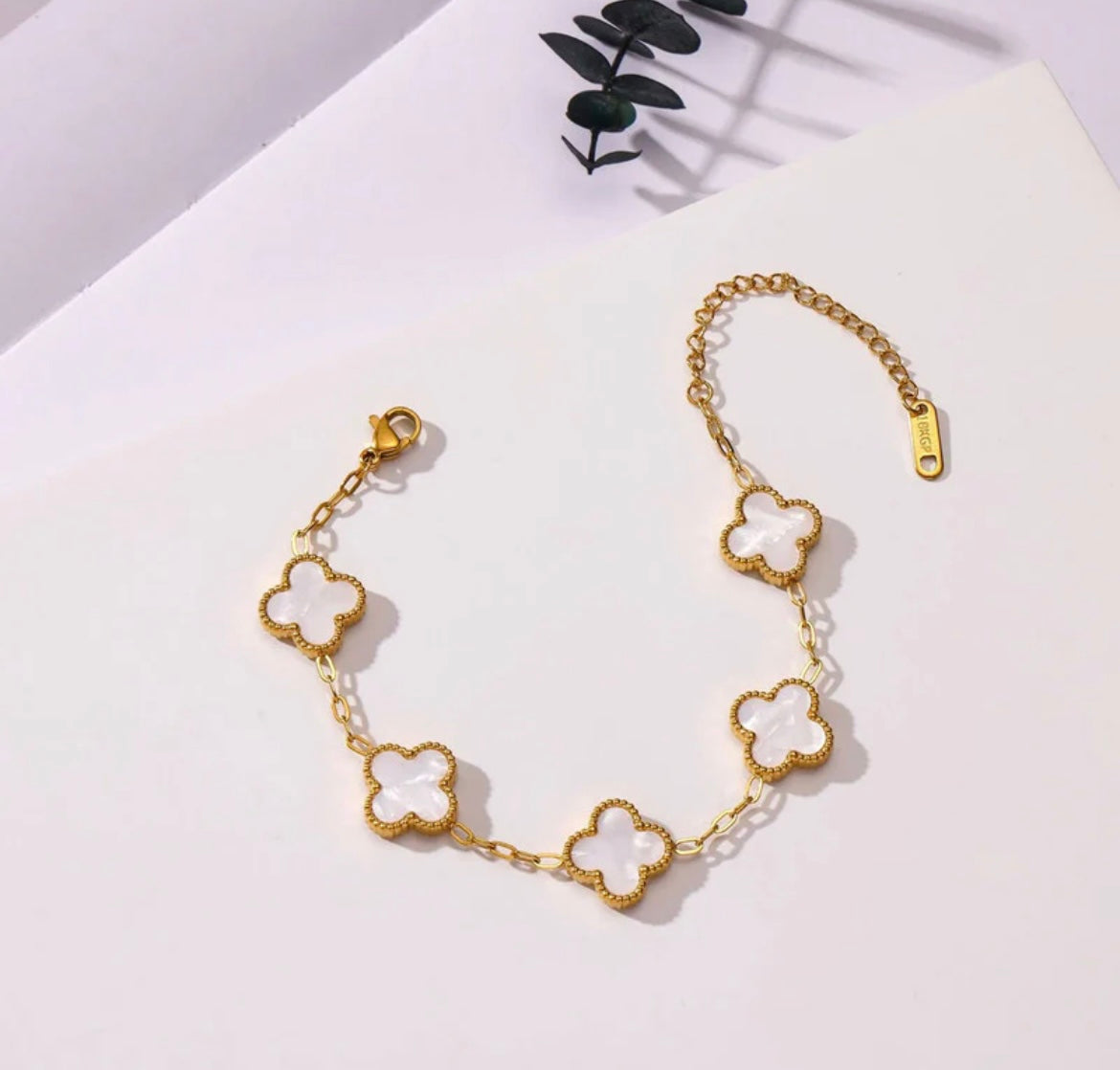 Gold chain bracelet with five white clover-shaped charms from ELL DESIGNS on white background