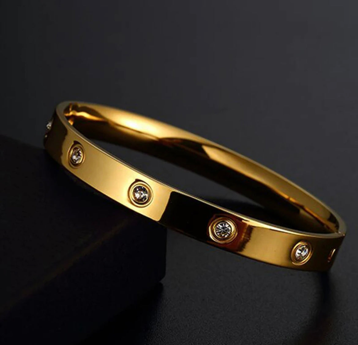 Elegant gold bangle bracelet with embedded clear gemstones by ELL DESIGNS on black background